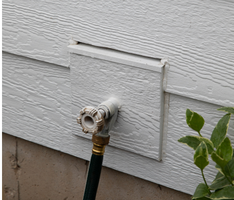 Cedar texture mini split on the exterior of a house with some hose pipe attached.