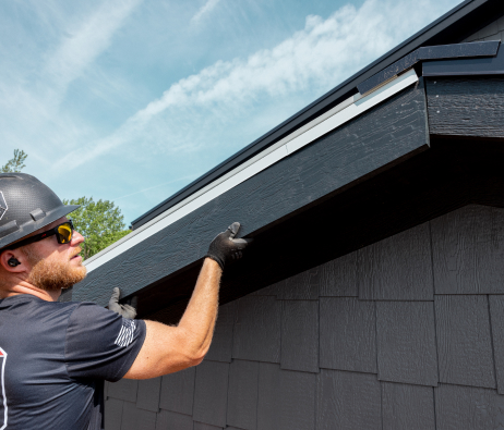 A worker in a hard hat lifting some trim up into place along a roofline.