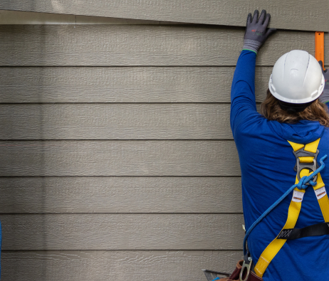 A worker in a hard hat putting up siding