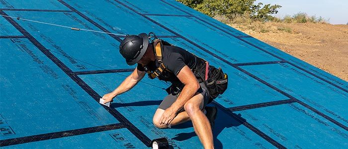 Builder on roof installing WeatherLogic Seam & Flashing Tape to panels